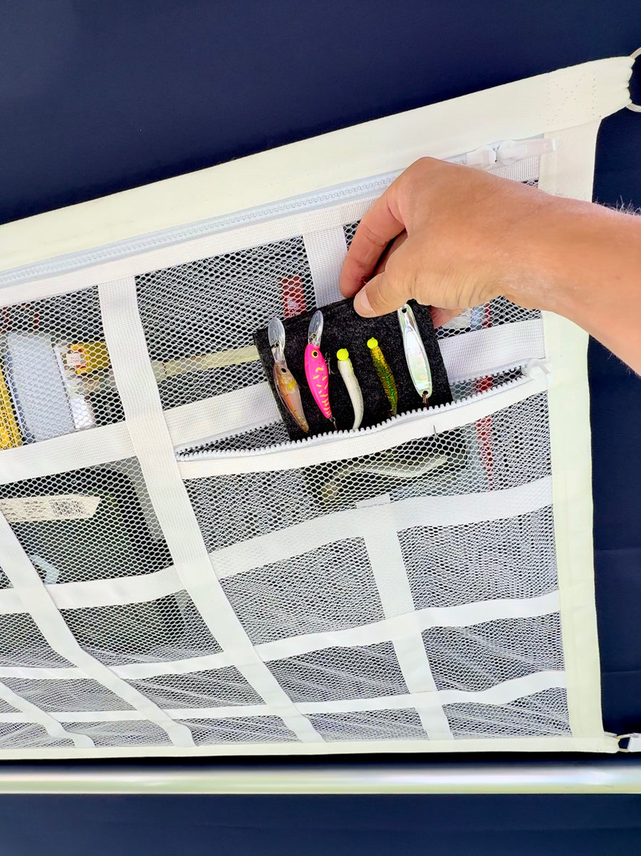 Hand placing a wallet of fishing lures into a zip pocket on the white ZBAD1 marine cargo net