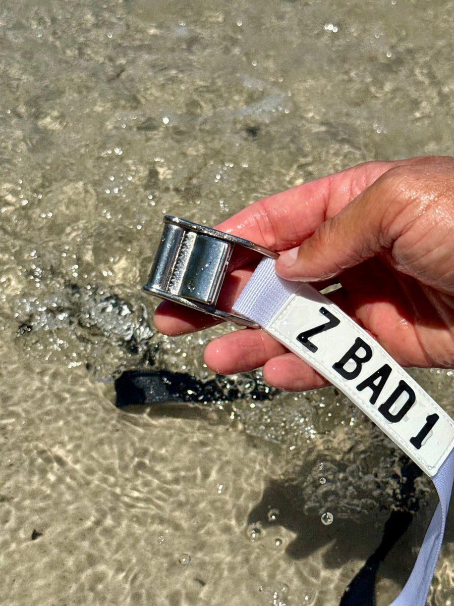 Stainless steel cam buckle on a white ZBAD1 marine tension strap held over shallow water