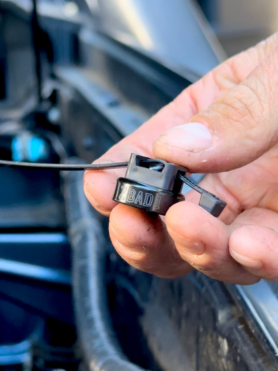 ZBAD1 magnet cable tie holder held in hand with a cable tie routing a wire in an engine bay