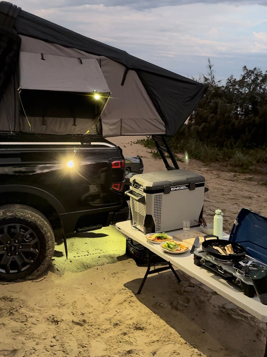 ZBAD1 magnetic multi torch lighting a beach campsite at dusk beside a ute with rooftop tent