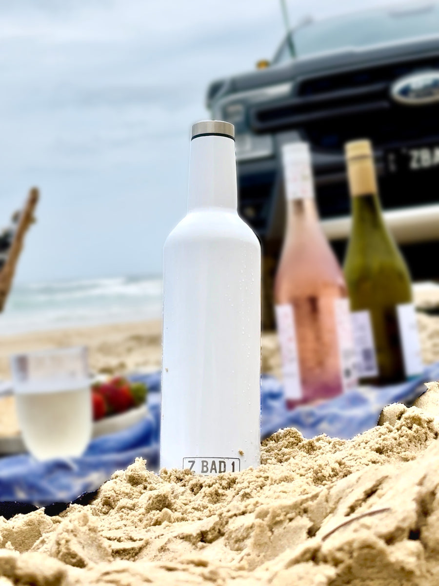 White ZBAD1 insulated flask in the sand at a beach picnic with wine bottles and a 4WD behind