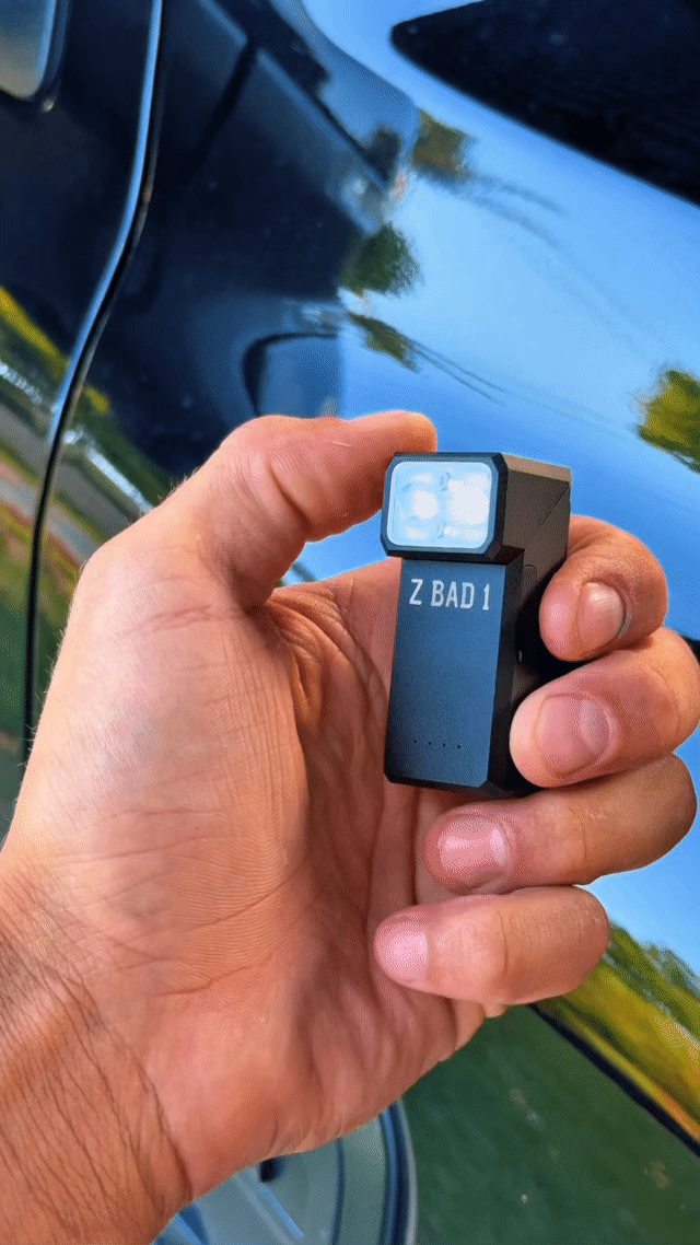 ZBAD1 magnetic multi torch held in hand with white LED lit, beside a vehicle