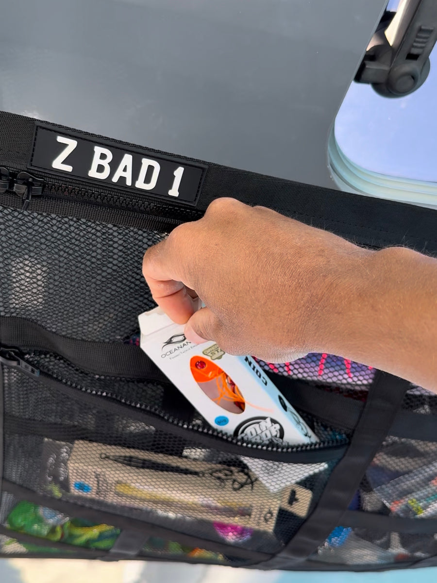 Hand taking a boxed fishing lure out of a zip pocket on the black ZBAD1 marine grade cargo net