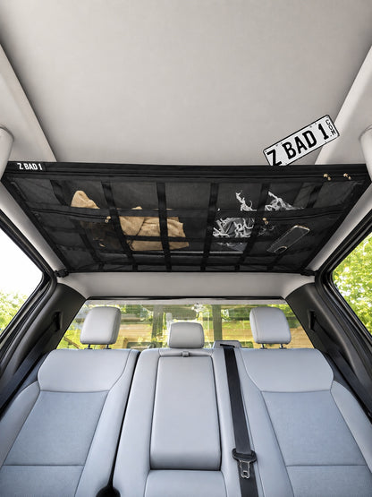 ZBAD1 American truck roof net mounted to the interior ceiling of a pickup cab, storing bags and clothes