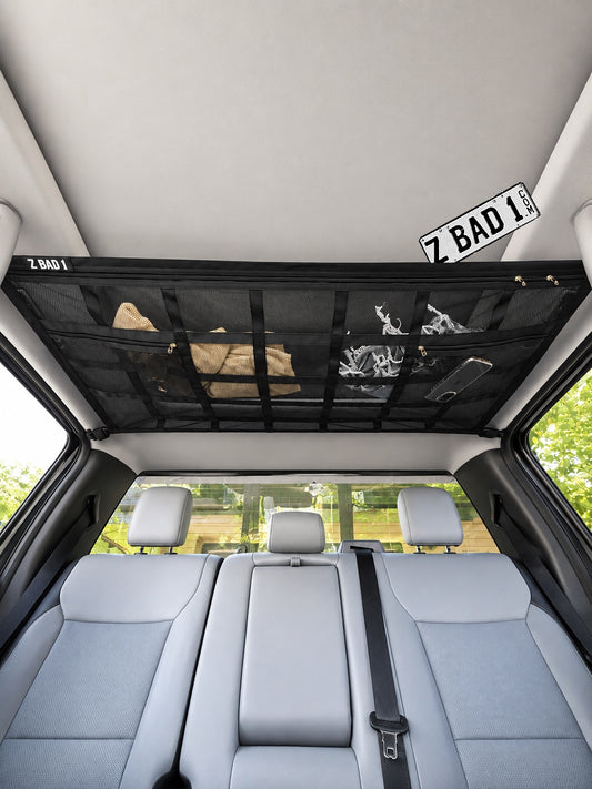ZBAD1 American truck roof net mounted to the interior ceiling of a pickup cab, storing bags and clothes