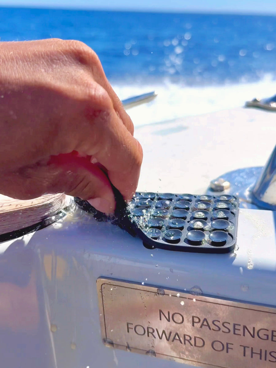 Hand peeling a black ZBAD1 grip mat off a smooth boat surface, showing suction pods